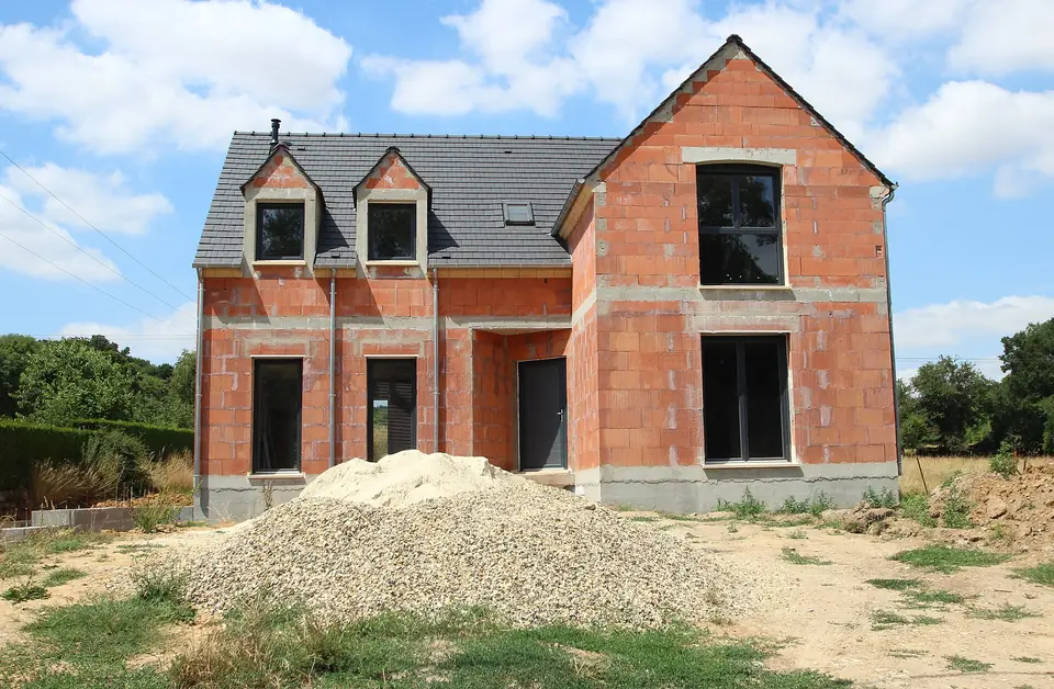 Maison individuelle en construction à Guignecourt, murs en briques creuses montés, toiture couverte et tas de gravier devant le chantier.